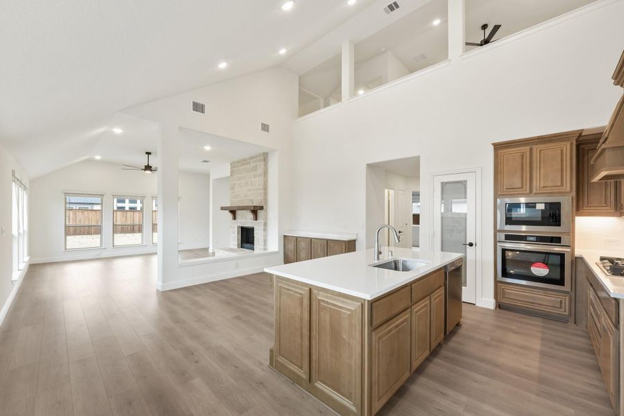 Open-concept kitchen with large island, wood cabinets, and stainless appliances flowing into living room with fireplace Open-concept kitchen with large island, wood cabinets, and stainless appliances flowing into living room with fireplace
