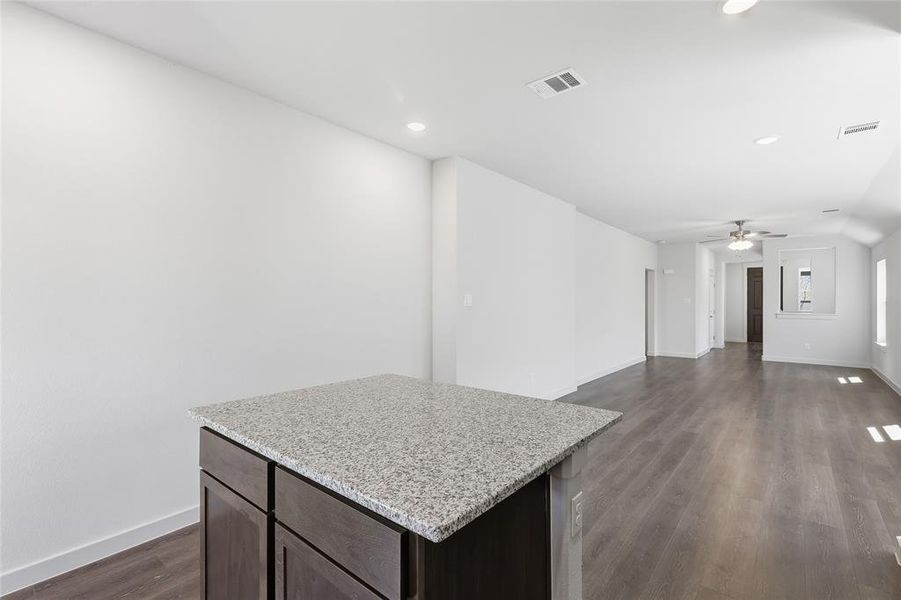 Kitchen featuring dark wood-style flooring, a kitchen island, light stone countertops, dark wood finish cabinets, and open floor plan