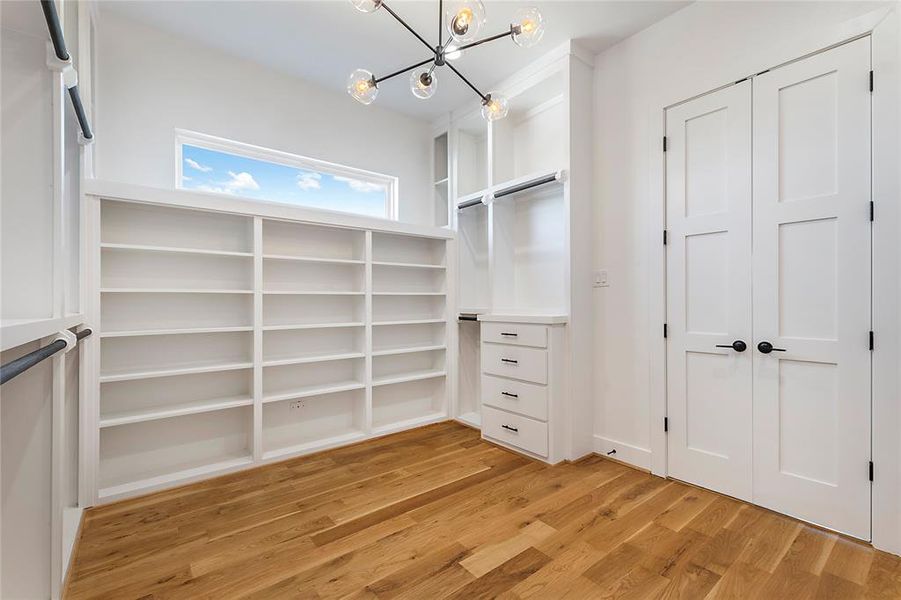 Walk in closet with light wood-type flooring and a notable chandelier