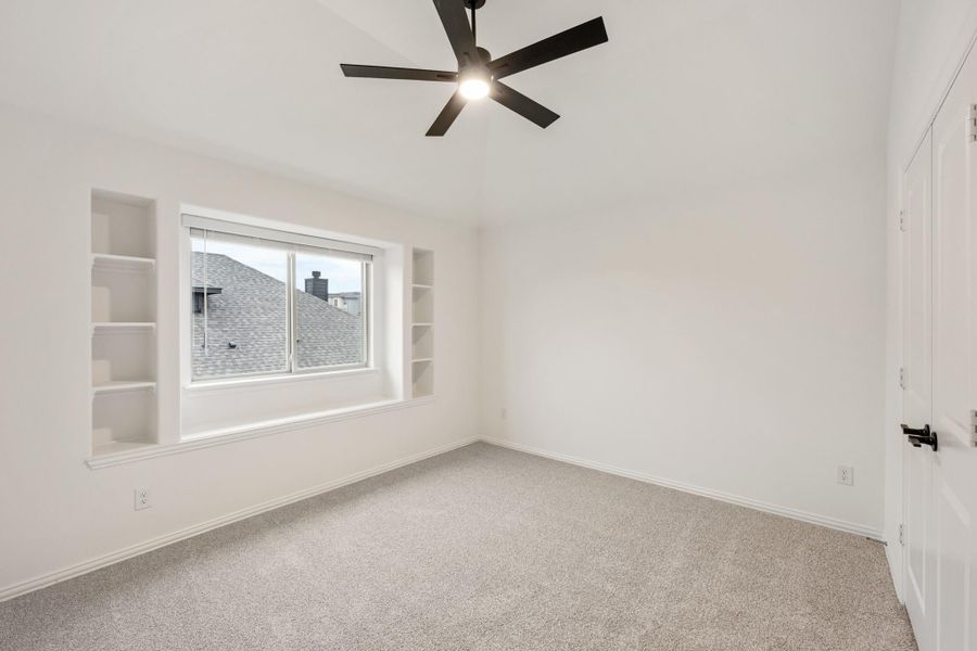 Empty bedroom with carpet, ceiling fan, window, and built-in shelves on each side Empty bedroom with carpet, ceiling fan, window, and built-in shelves on each side