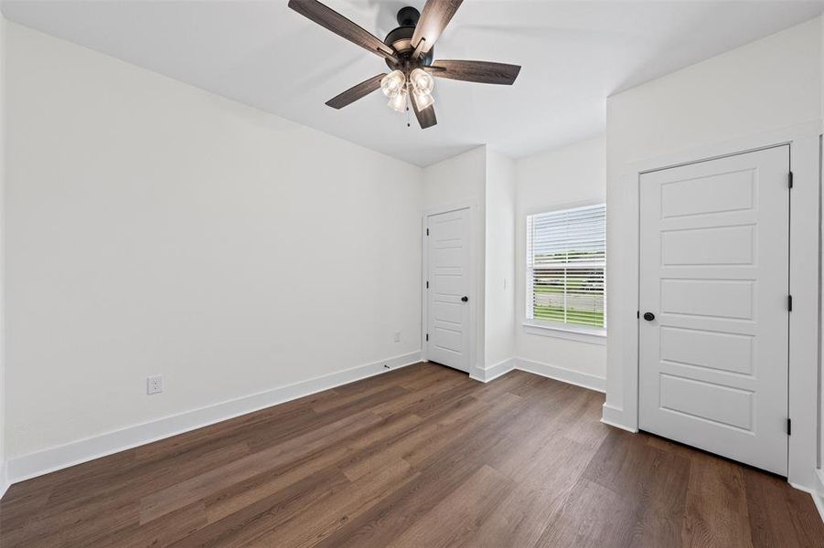 This room features hardwood flooring, white walls, and a ceiling fan with light fixture
