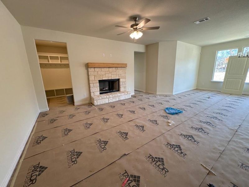 Unfurnished living room featuring a stone fireplace and a ceiling fan