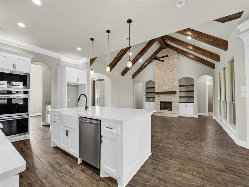 Kitchen featuring dark wood-type flooring, white cabinets, a fireplace, and vaulted ceiling with beams