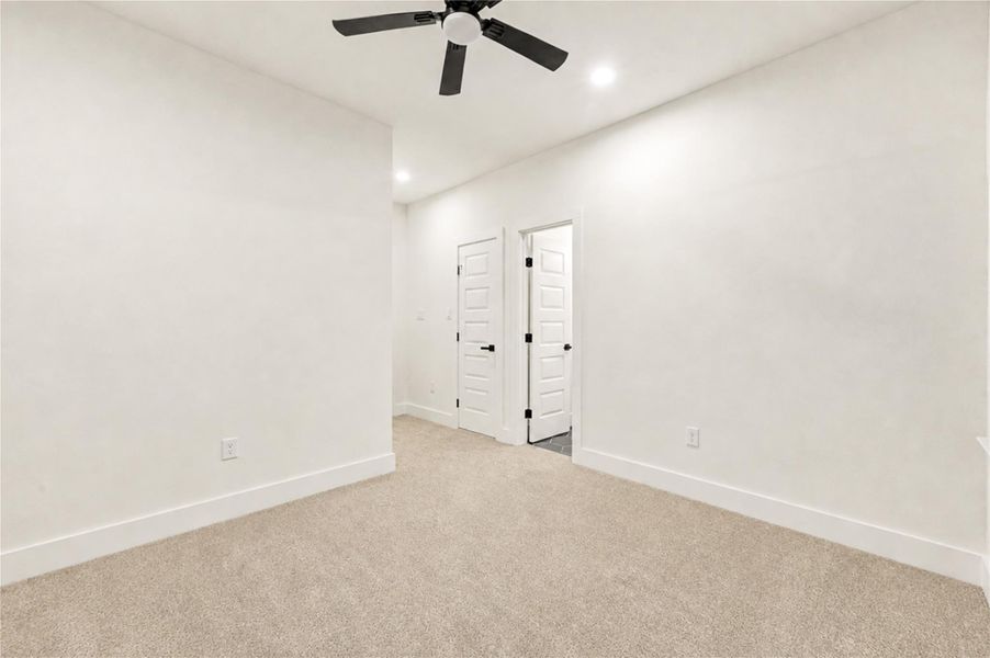 Bright and spacious 2nd bedroom with soft carpet, modern ceiling fan, and sleek white doors, offering a comfortable and inviting atmosphere.