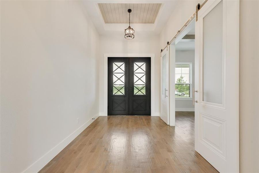 Entrance foyer with a tray ceiling, light hardwood / wood-style flooring, and a barn door