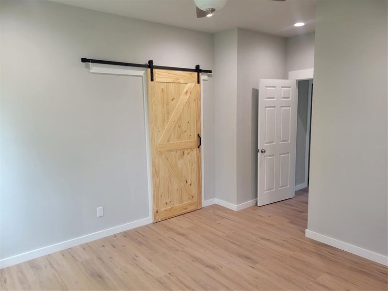 Interior room featuring light-toned wood-finish flooring, a natural wood sliding barn door with black hardware, and light gray painted walls