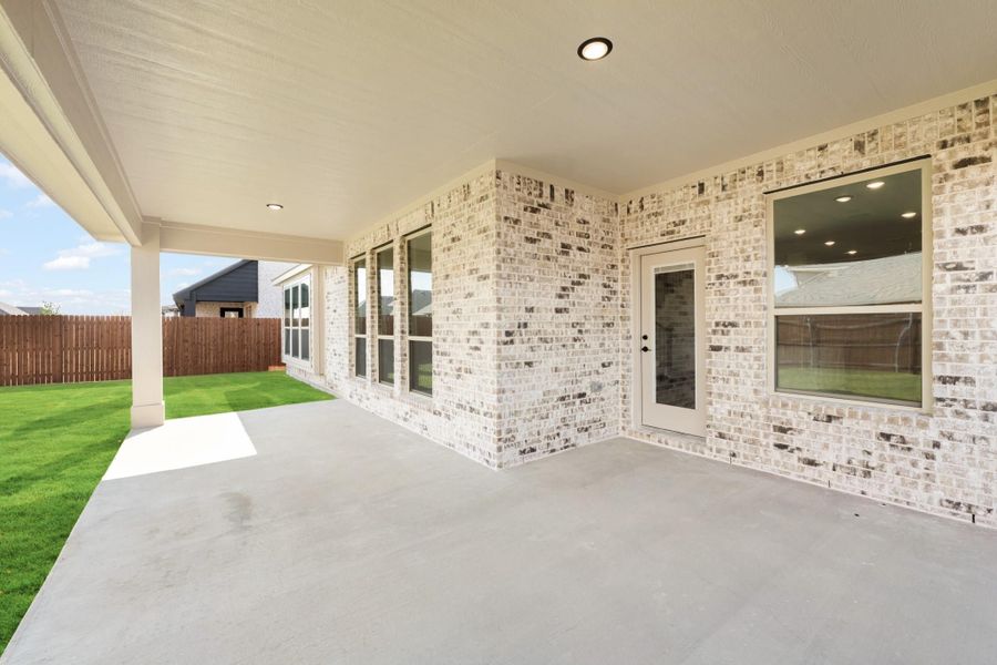 Covered back patio with concrete floor, light brick exterior, back door, and fenced yard with green lawn.