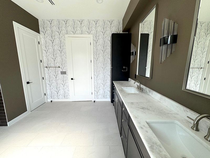 Full bathroom featuring double vanity, wallpapered walls, baseboards, and a sink