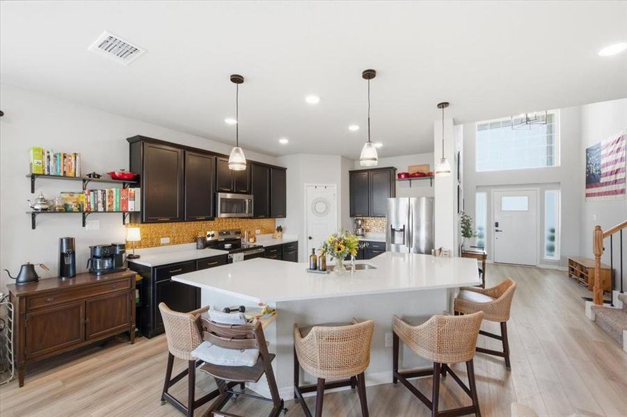 Kitchen with a kitchen breakfast bar, a spacious island, chic and decorative backsplash, light wood finished floors, and stainless steel appliances Kitchen with a kitchen breakfast bar, a spacious island, chic and decorative backsplash, light wood finished floors, and stainless steel appliances