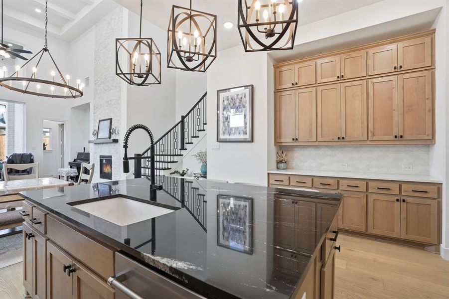 Kitchen featuring light wood-type flooring, dark stone countertops, light brown cabinets, decorative light fixtures, and a towering ceiling Kitchen featuring light wood-type flooring, dark stone countertops, light brown cabinets, decorative light fixtures, and a towering ceiling