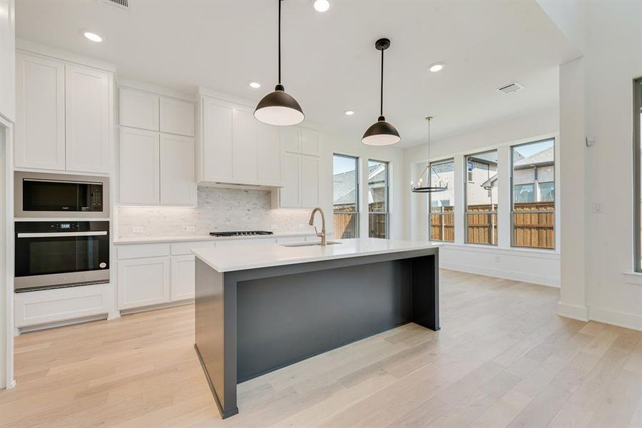 Kitchen featuring backsplash, white cabinets, oven, decorative light fixtures, and healthy amount of natural light