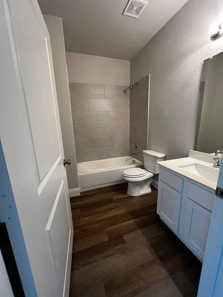 Full bathroom with vanity, hardwood / wood-style floors, tiled shower / bath, and toilet