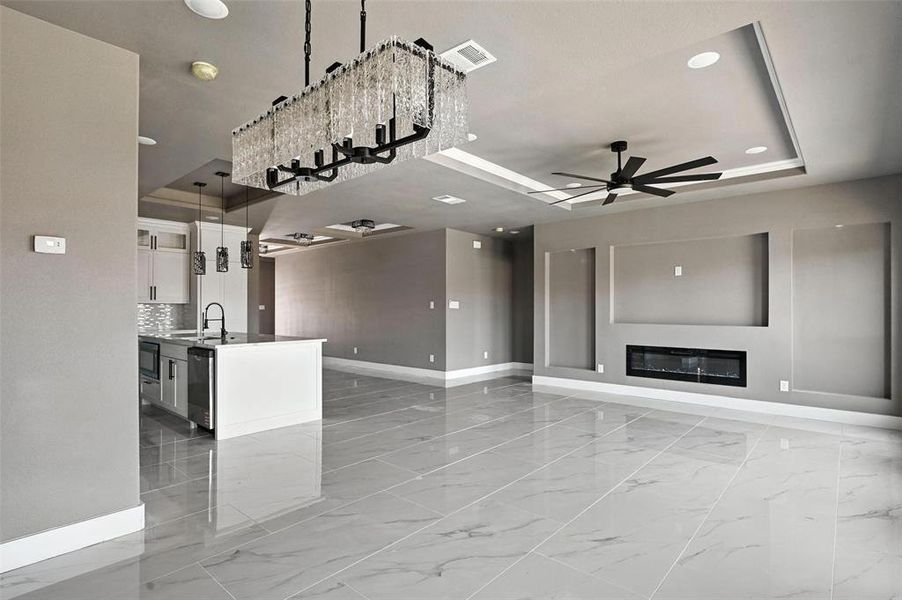 Unfurnished living room with a tray ceiling, a ceiling fan, light marble finish flooring, a glass covered fireplace, and recessed lighting Unfurnished living room with a tray ceiling, a ceiling fan, light marble finish flooring, a glass covered fireplace, and recessed lighting