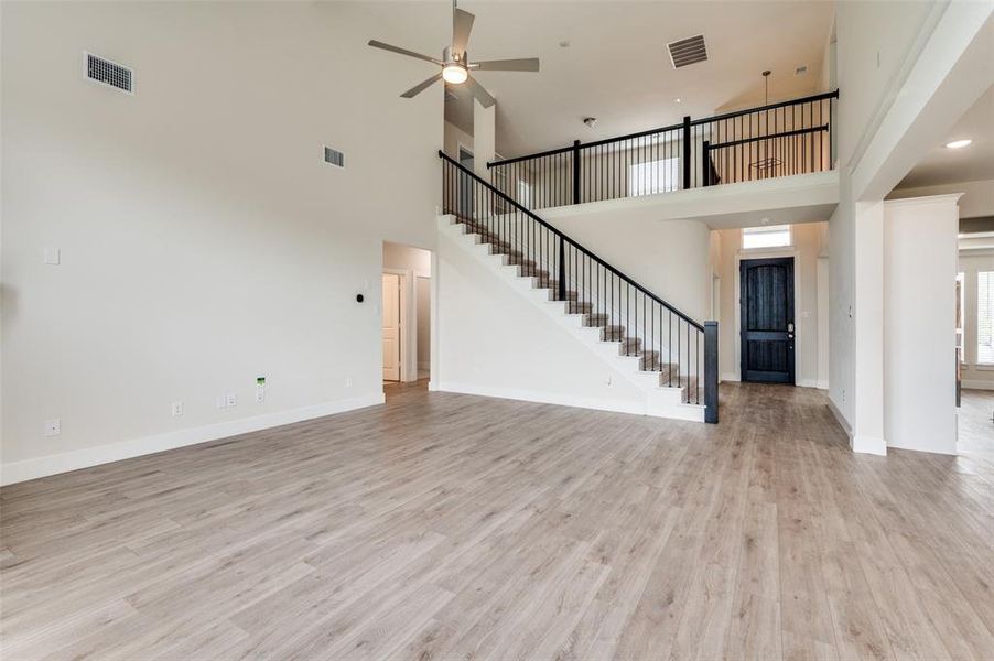 Unfurnished living room featuring stairs, a towering ceiling, ceiling fan, light wood-style floors, and baseboards Unfurnished living room featuring stairs, a towering ceiling, ceiling fan, light wood-style floors, and baseboards