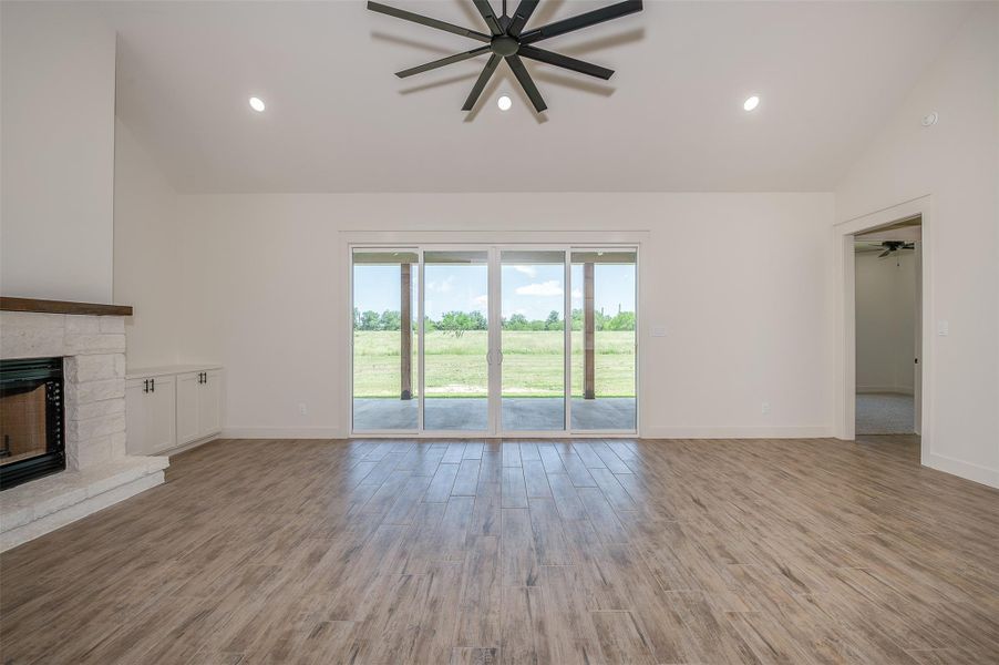 Unfurnished living room featuring lofted ceiling, a ceiling fan, light wood finished floors, a fireplace, and recessed lighting