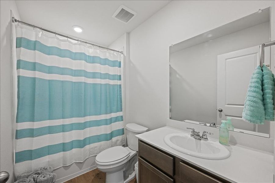 Bathroom featuring shower / tub combo with curtain, vanity, and dark wood-style floors Bathroom featuring shower / tub combo with curtain, vanity, and dark wood-style floors