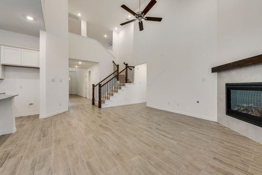 Unfurnished living room with a fireplace, a towering ceiling, ceiling fan, and light hardwood / wood-style flooring