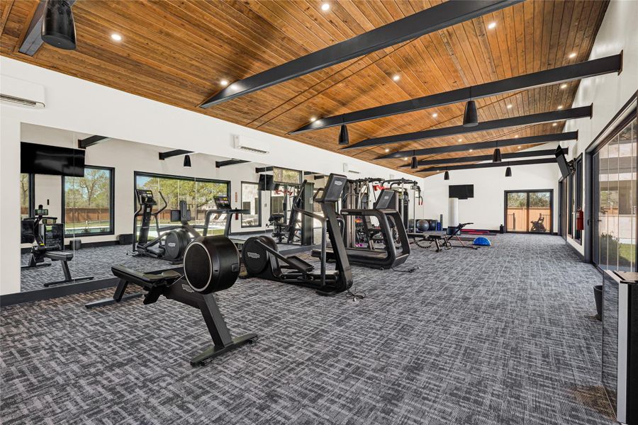 Gym features a spacious interior with high ceilings and wood paneling. It is equipped with a variety of exercise machines and large windows for natural light, creating an inviting workout environment.