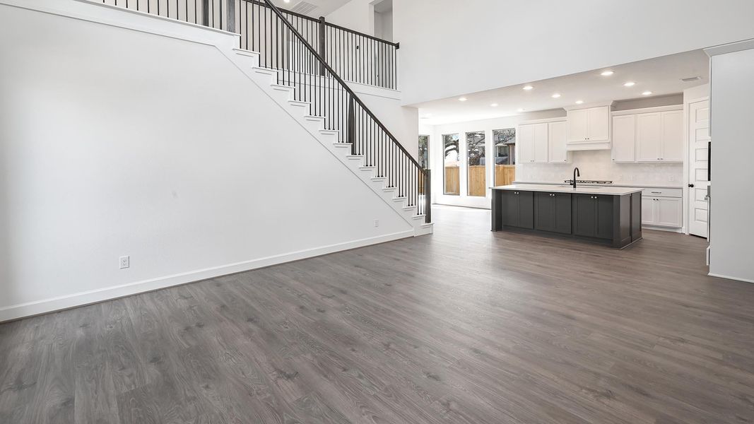Unfurnished living room featuring dark wood finished floors, recessed lighting, a high ceiling, and stairs