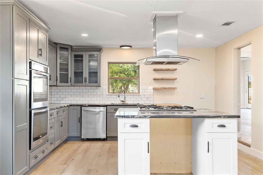 Kitchen featuring light wood finished floors, island exhaust hood, plenty of natural light, backsplash, and recessed lighting Kitchen featuring light wood finished floors, island exhaust hood, plenty of natural light, backsplash, and recessed lighting