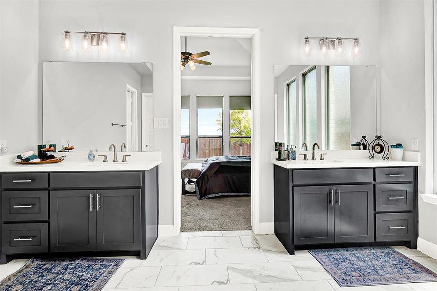 Full bath featuring two vanities, light marble finish flooring, a ceiling fan, and ensuite bathroom