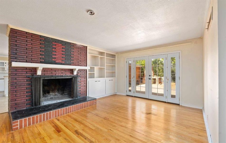 Unfurnished living room with a textured ceiling, built in shelves, a brick fireplace, light wood-style flooring, and french doors