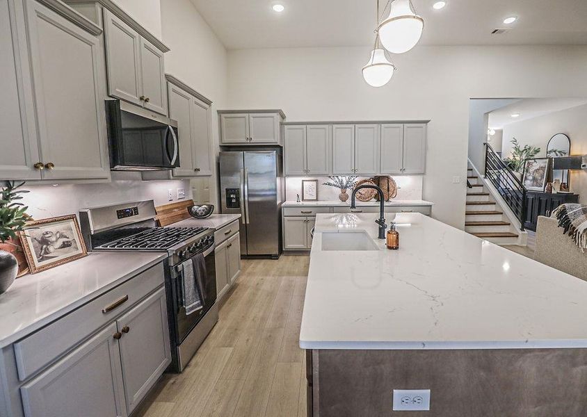 Kitchen with gray cabinetry, stainless steel appliances, an island with sink, and decorative light fixtures