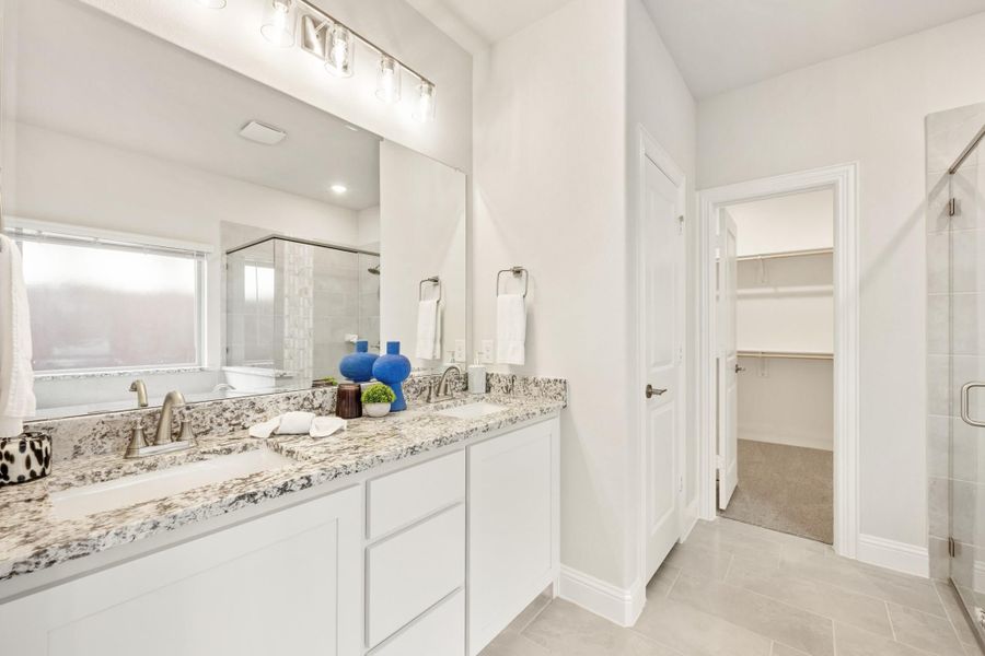 Bathroom with double vanity, granite countertops, glass shower, and walk-in closet entrance