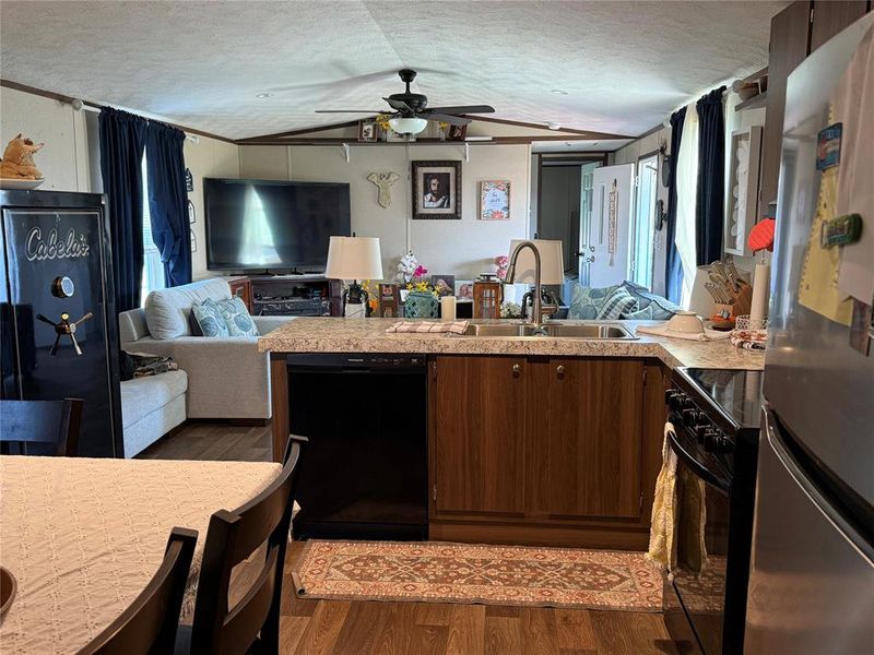Kitchen featuring open floor plan, black appliances, light countertops, a peninsula, and dark wood-style flooring