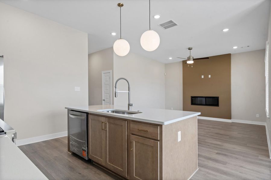 Kitchen island featuring an integrated sink, stainless steel dishwasher, and light wood-finish cabinetry