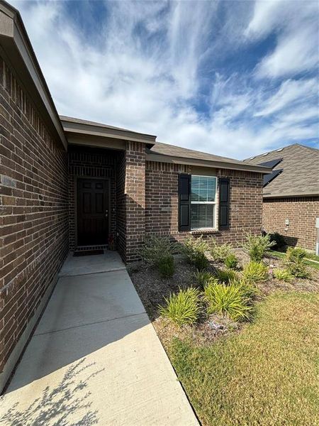 View of exterior entry featuring brick siding and a yard