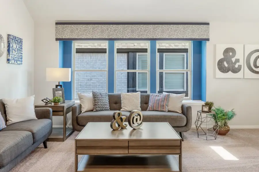 Living room with gray sofa, wood coffee table, and large blue-trimmed triple window with decorative valance