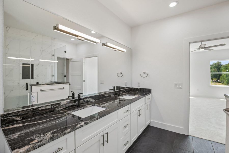 A spacious double vanity with bold dark stone countertops elevates this modern primary bathroom.