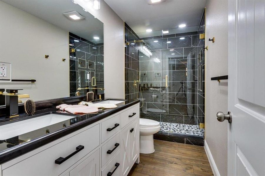 Bathroom with double vanity, dark wood finished floors, and a shower stall