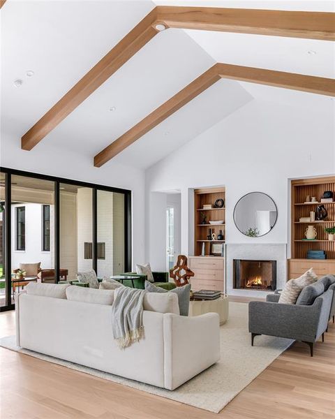 Living room with vaulted ceiling with beams, built in shelves, and light wood-type flooring