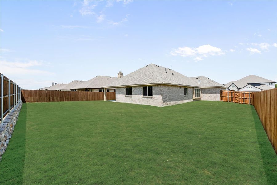 Backyard with large green lawn, wood privacy fence, and brick home with covered patio in background. Backyard with large green lawn, wood privacy fence, and brick home with covered patio in background.