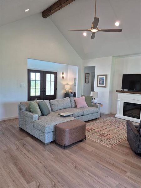 Living area with recessed lighting, high vaulted ceiling, beam ceiling, a glass covered fireplace, and light wood-style flooring