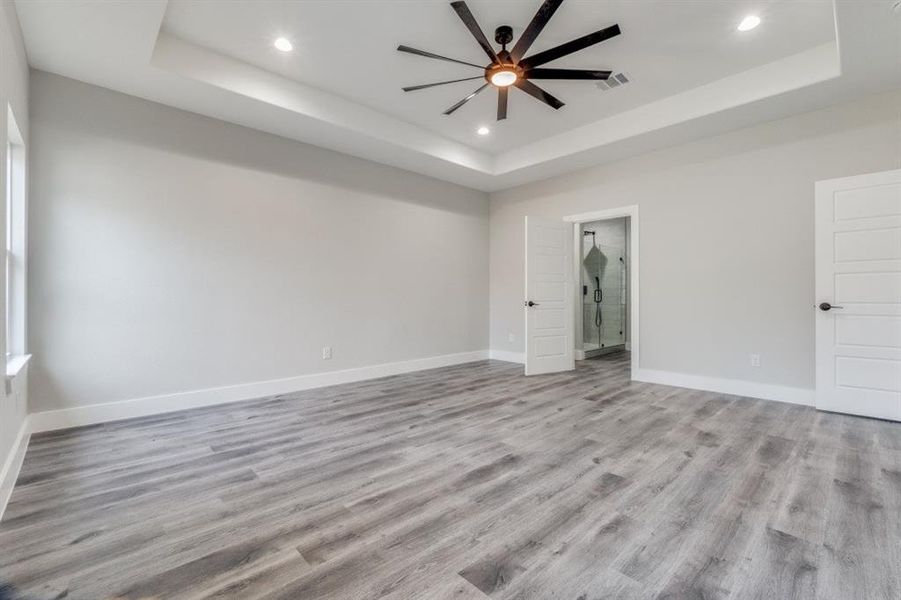 Empty room featuring ceiling fan, light hardwood / wood-style floors, and a tray ceiling