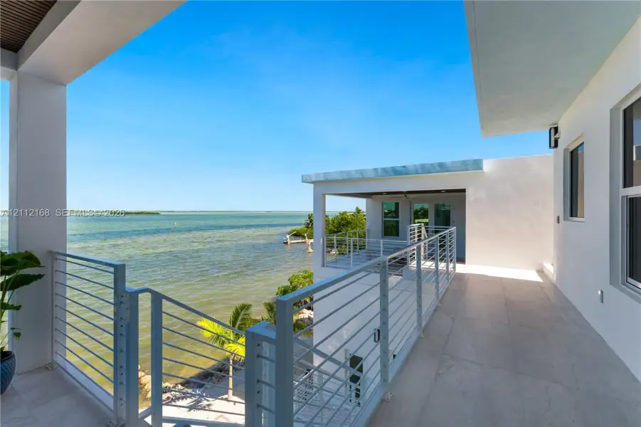 Covered waterfront balcony featuring large-format tile flooring, white metal cable railing, and a tongue-and-groove wood-finish ceiling Covered waterfront balcony featuring large-format tile flooring, white metal cable railing, and a tongue-and-groove wood-finish ceiling