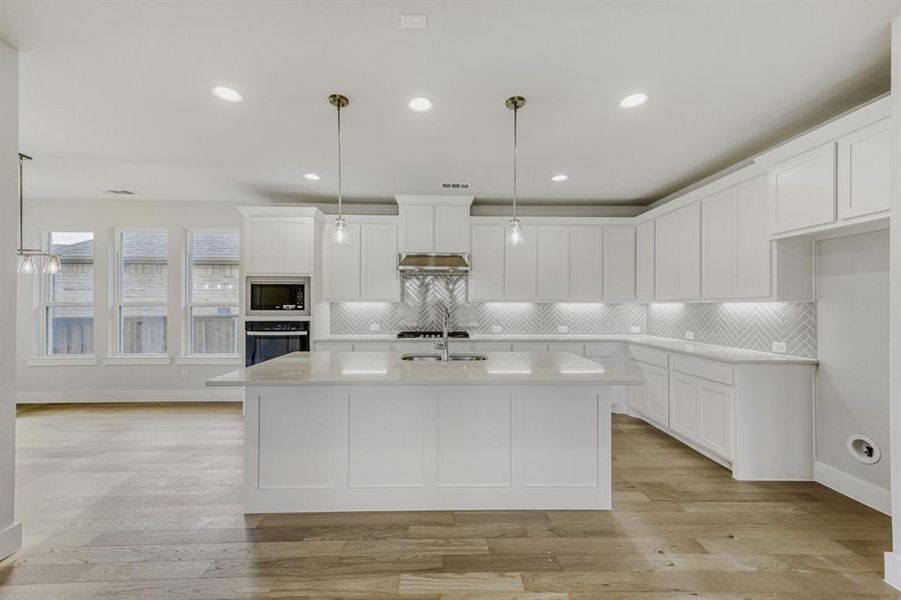 Kitchen featuring pendant lighting, white cabinets, stainless steel appliances, light wood finished floors, and a center island with sink