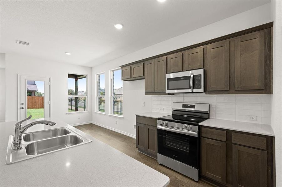 Kitchen featuring sink, backsplash, stainless steel appliances, dark brown cabinetry, and dark wood-type flooring