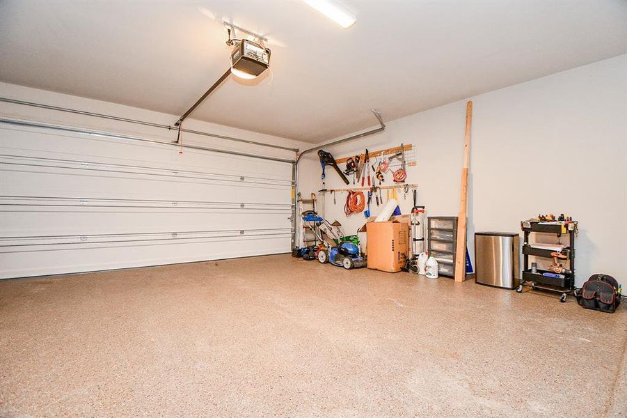 This spacious garage features a clean, epoxy-coated floor, ample storage with wall-mounted racks, and room for tools and equipment. Perfect for a workshop or parking.