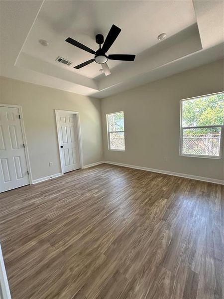 Unfurnished bedroom with a raised ceiling, wood finished floors, and a ceiling fan