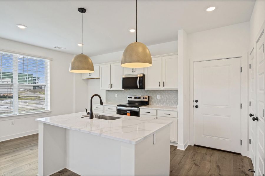 Kitchen featuring a center island with sink, white shaker cabinetry, stainless steel appliances, pendant lighting, and wood-finish flooring