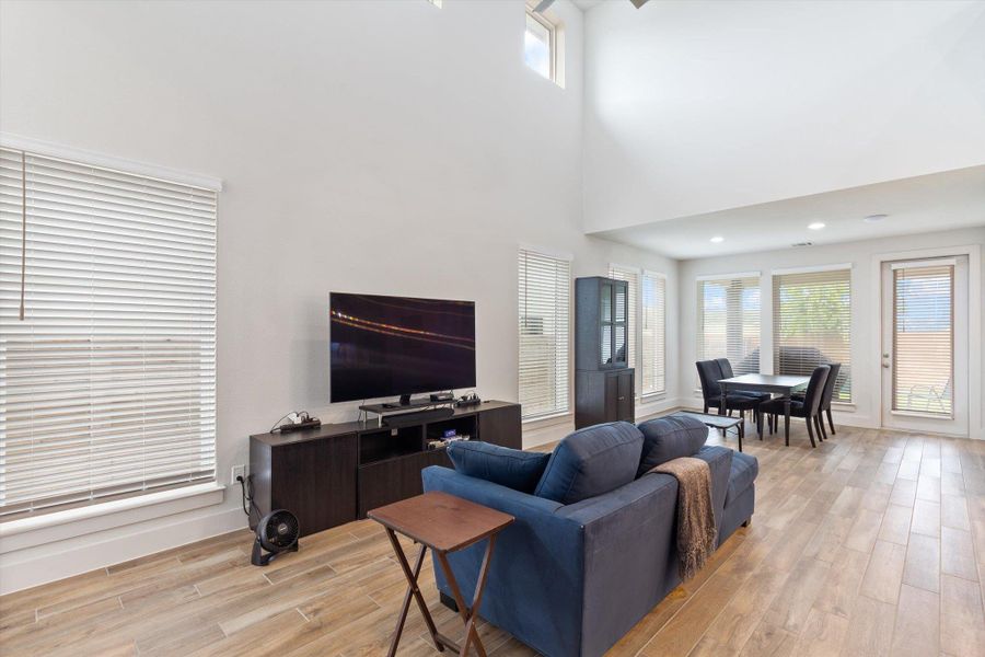 Living room featuring light wood-style flooring, a towering ceiling, and recessed lighting