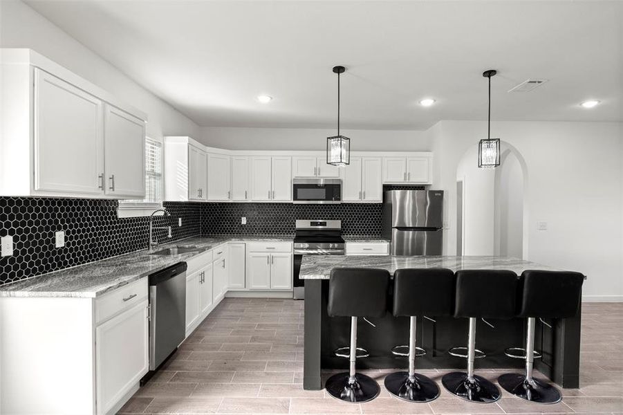 Kitchen featuring light stone countertops, a breakfast bar, white cabinetry, stainless steel appliances, and pendant lighting