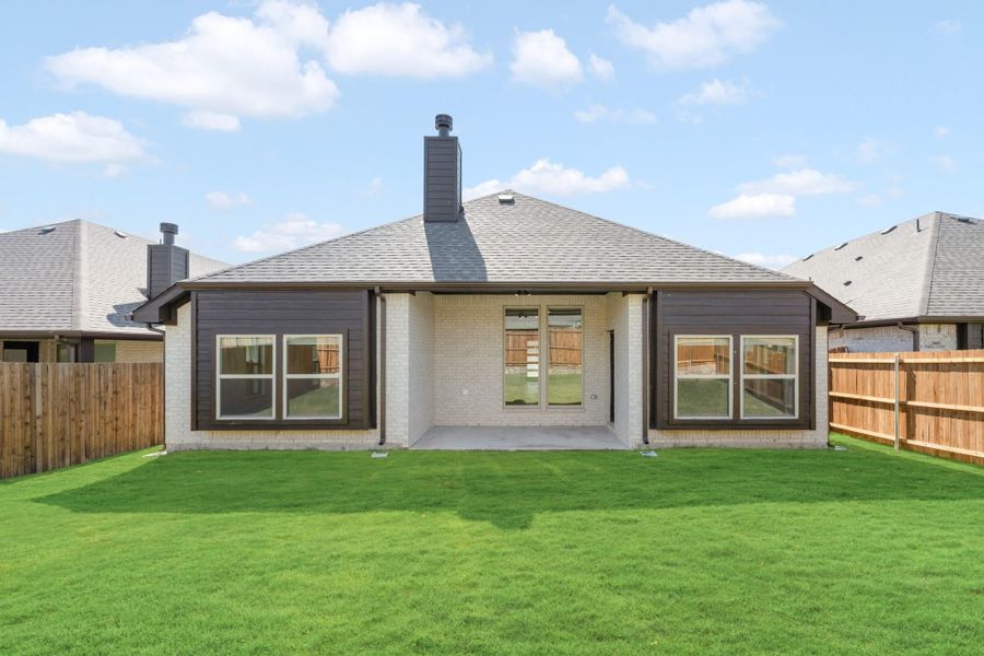 Rear exterior of single-story home with brick and dark siding, covered patio, large windows, and fenced backyard with green lawn.
