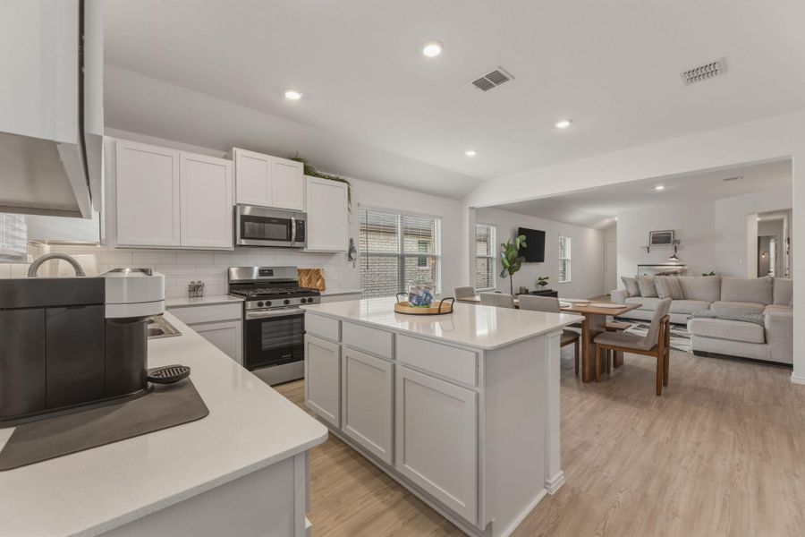 The kitchen features white cabinetry, stainless steel appliances, a white subway tile backsplash, and a central island with a white countertop