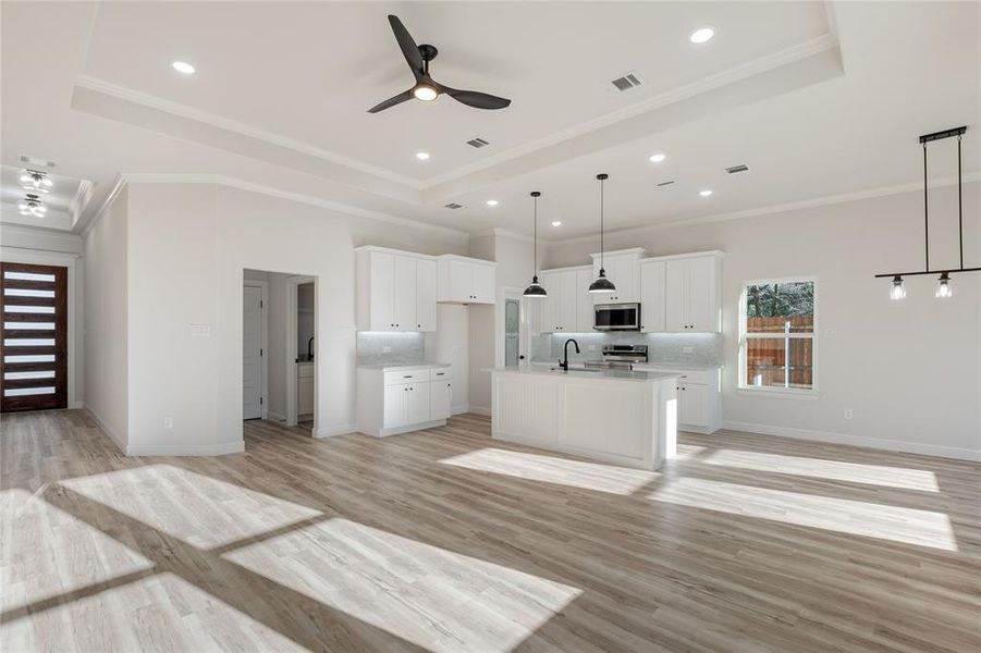 Entrance and living room with a tray ceiling, crown molding, ceiling fan, light wood-style floors, and recessed lighting.