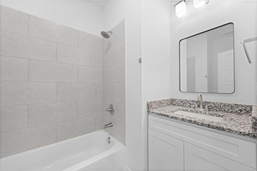 BFull bathroom featuring tiled tub/shower combo, granite countertop vanity, and modern fixtures with clean, bright finishes.